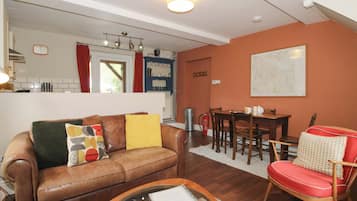 A living room with a brown leather sofa, a glass coffee table, a red chair, a dining table with chairs, a kitchen area with a window, and a map on the wall.