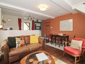 A living room with a brown leather sofa, a glass coffee table, a red chair, a dining table with chairs, a kitchen area with a window, and a map on the wall. - Little Pentwyn (Hereford)