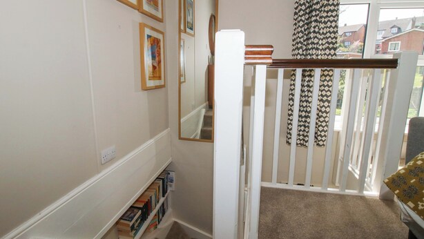 Un escalier avec une rampe blanche, une bibliothèque et un miroir au mur.