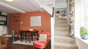 Un escalier dont les marches sont recouvertes de moquette, un coin repas avec une table et des chaises en bois, et une bibliothèque adossée au mur.