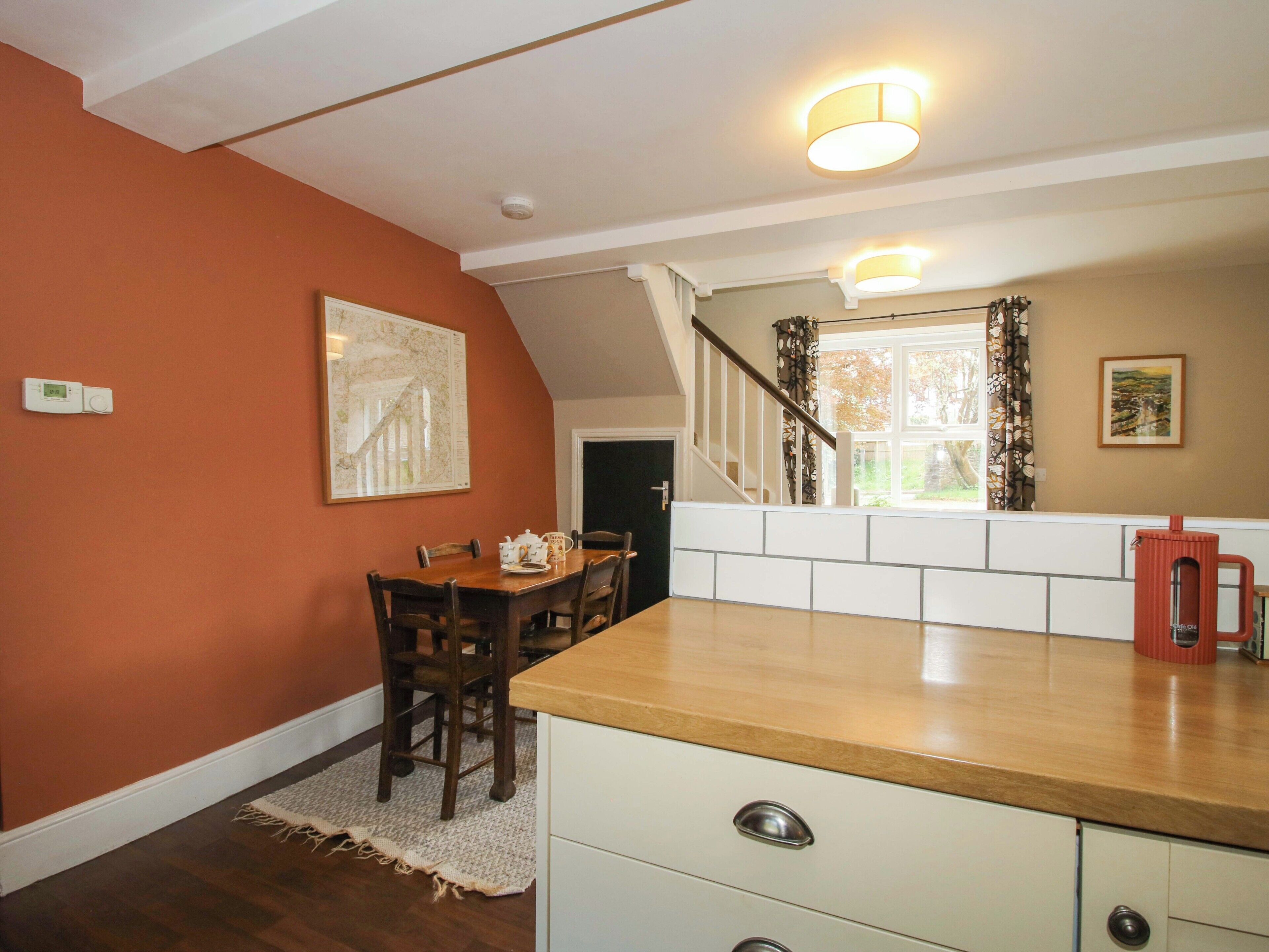 A dining area with a wooden table and chairs, a kitchen counter, and a staircase leading to another level.
