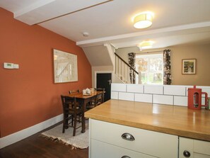 A dining area with a wooden table and chairs, a kitchen counter, and a staircase leading to another level. - Little Pentwyn (Hereford)