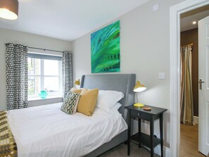 A neatly made bed with white linens, a gray headboard, and a bedside table with a lamp. - Little Pentwyn (Hereford)