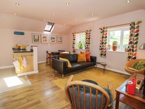 A living room with a sofa, a dining table, and a kitchen area with a counter and a window. - Pentwyn Barn (Hereford)