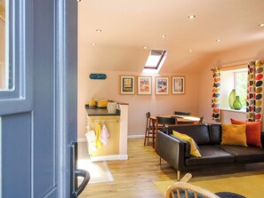 A cozy living room with a sofa, a dining table, and a kitchen area with a countertop. - Pentwyn Barn (Hereford)