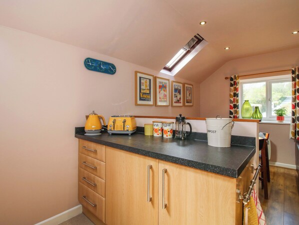 A kitchen with wooden cabinets, a black countertop, a coffee maker, a kettle, and vintage posters on the wall.