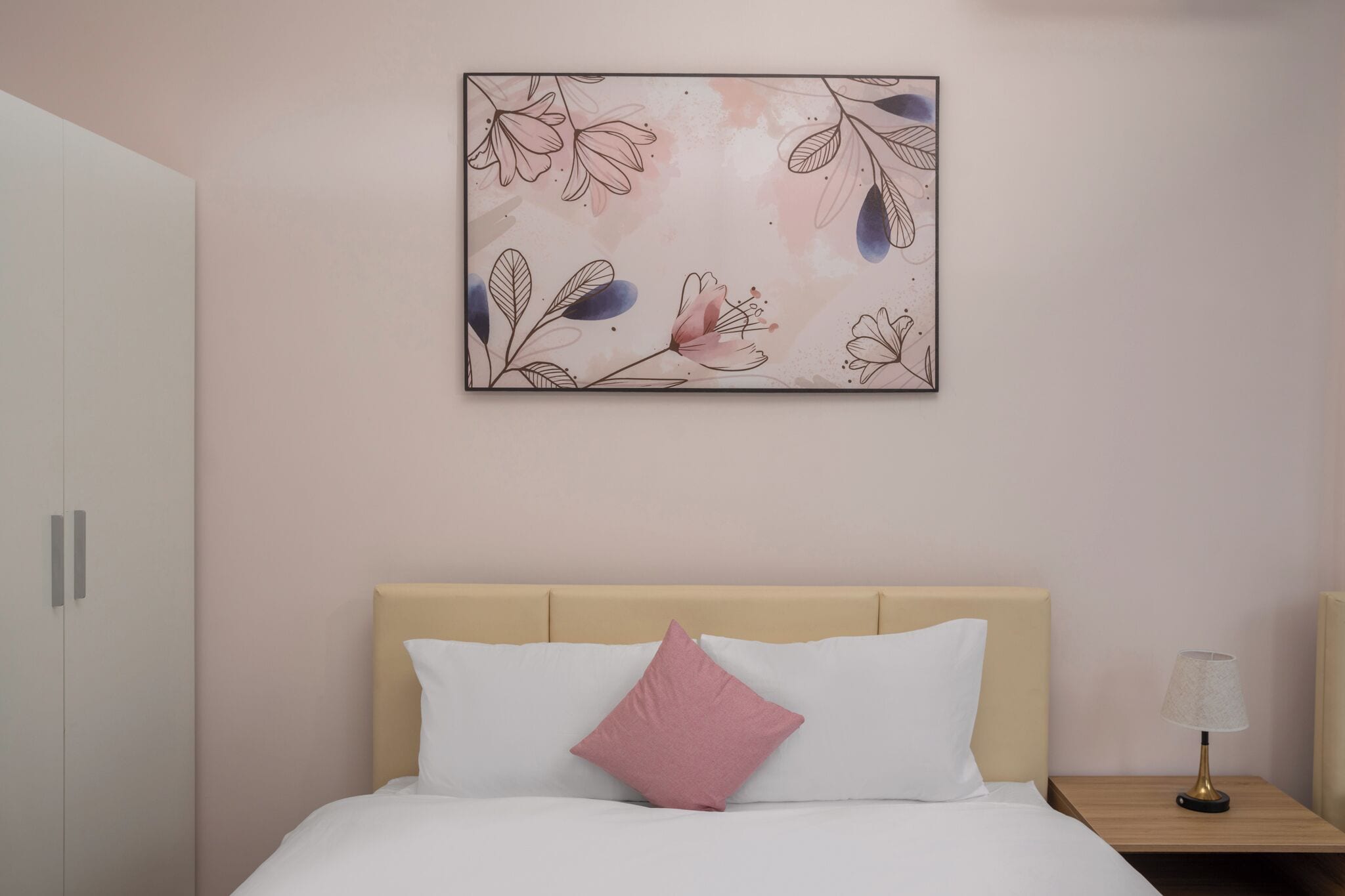 Un dormitorio con cama, mesita de noche, lámpara y una obra de arte colgada en la pared.