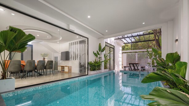 An indoor swimming pool with clear blue water, surrounded by modern furniture and large green plants. - Cam On Luxury Pool 4BR Villa by the Beach (Da Nang)