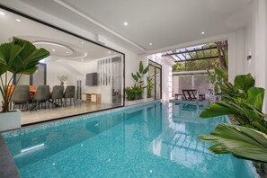 Ein Innenpool mit klarem, blauem Wasser, umgeben von modernen Möbeln und großen Grünpflanzen.