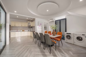 A modern kitchen with white cabinets, a dining table with chairs, and a built-in washing machine. - Cam On Luxury Pool 4BR Villa by the Beach (An Hai)
