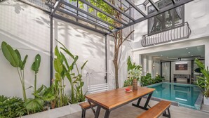 A modern outdoor dining area with a pool, surrounded by lush greenery and a metal pergola. - Cam On Luxury Pool 4BR Villa by the Beach (Da Nang)