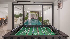 A foosball table with a view of a swimming pool and outdoor seating area. - Cam On Luxury Pool 4BR Villa by the Beach (Da Nang)
