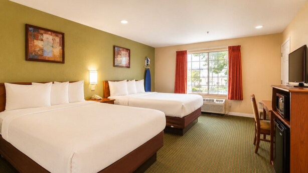 Ein Hotelzimmer mit zwei Betten, einem Schreibtisch mit Fernseher, einem Fenster mit Vorhängen und Bildern an den Wänden.