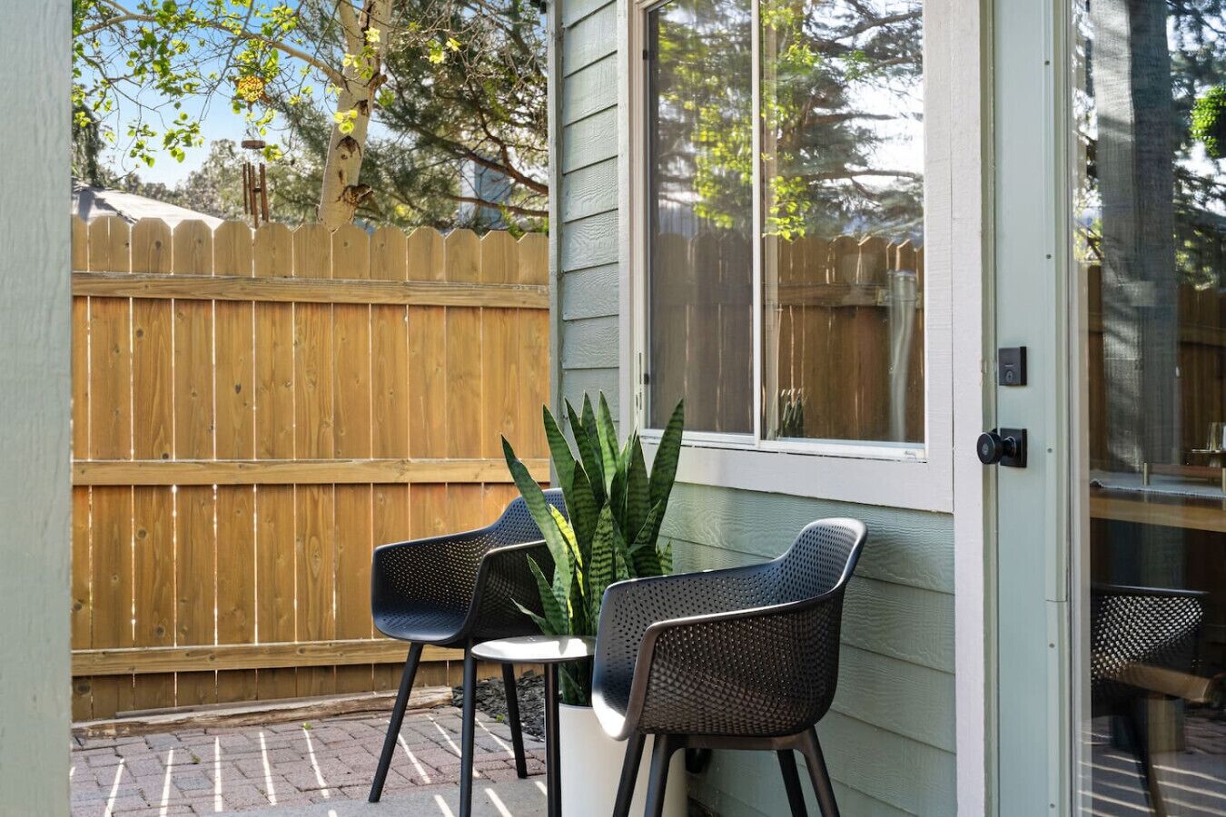 A patio with two chairs, a potted plant, and a wooden fence.