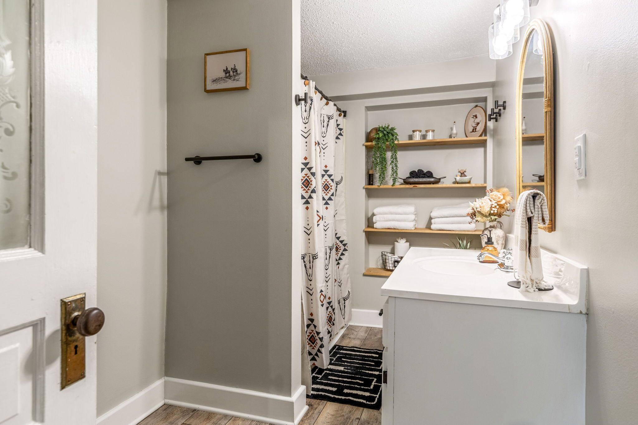 A bathroom with a shower, a sink with a mirror, shelves with towels, and a door with a keyhole.