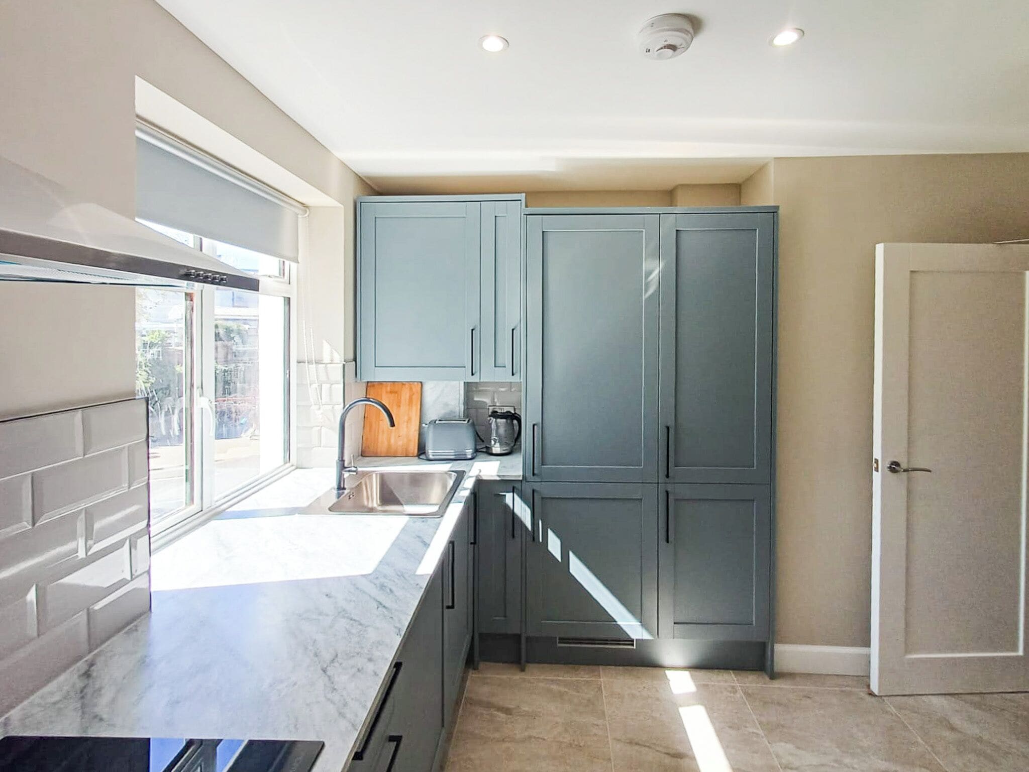 A modern kitchen with grey cabinets, a marble countertop, and a window.
