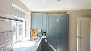 A modern kitchen with grey cabinets, a marble countertop, and a window. - Harbour View Apartments Portsmouth (Portsmouth)