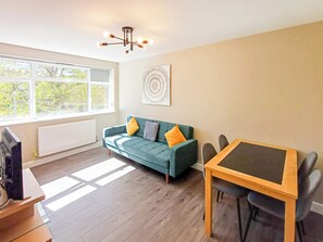 Una sala de estar con sofá, mesa, televisión y ventana con vista a árboles.