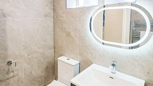 A bathroom with a toilet, a sink, a mirror, and a window. - Harbour View Apartments Portsmouth (Portsmouth)