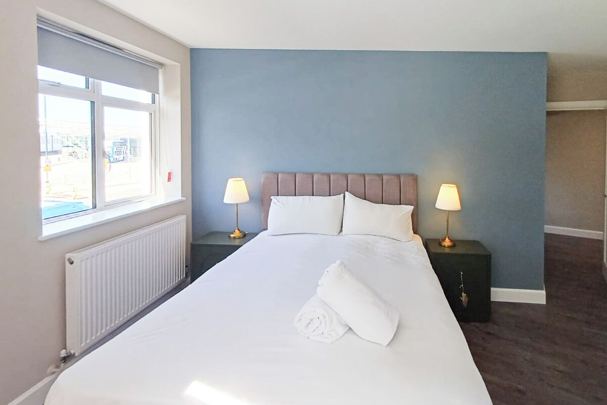 Een hotelkamer met een groot bed, twee nachtkastjes met lampen, een raam en een radiator.