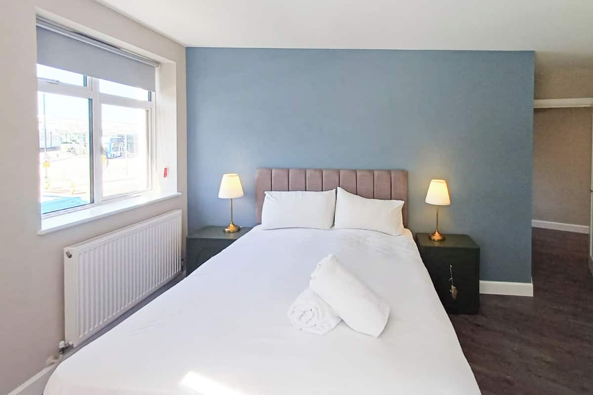 Una habitación de hotel con una cama grande, dos mesitas de noche con lámparas, una ventana y un radiador.