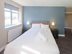 A hotel room with a large bed, two bedside tables with lamps, a window, and a radiator. - Harbour View Apartments Portsmouth (Portsmouth)