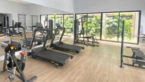 A gym with treadmills, weight machines, and a large window with a view of greenery. - Cozy Apartment - Prime Building (Campo Grande)