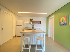 A compact kitchen with a central island, two stools, a refrigerator, and a gas stove.