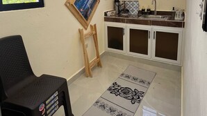 A compact kitchen with a window, a small stool, and a decorative mat.