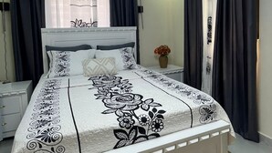 A bedroom with a bed, curtains, a nightstand, and a vase with flowers.