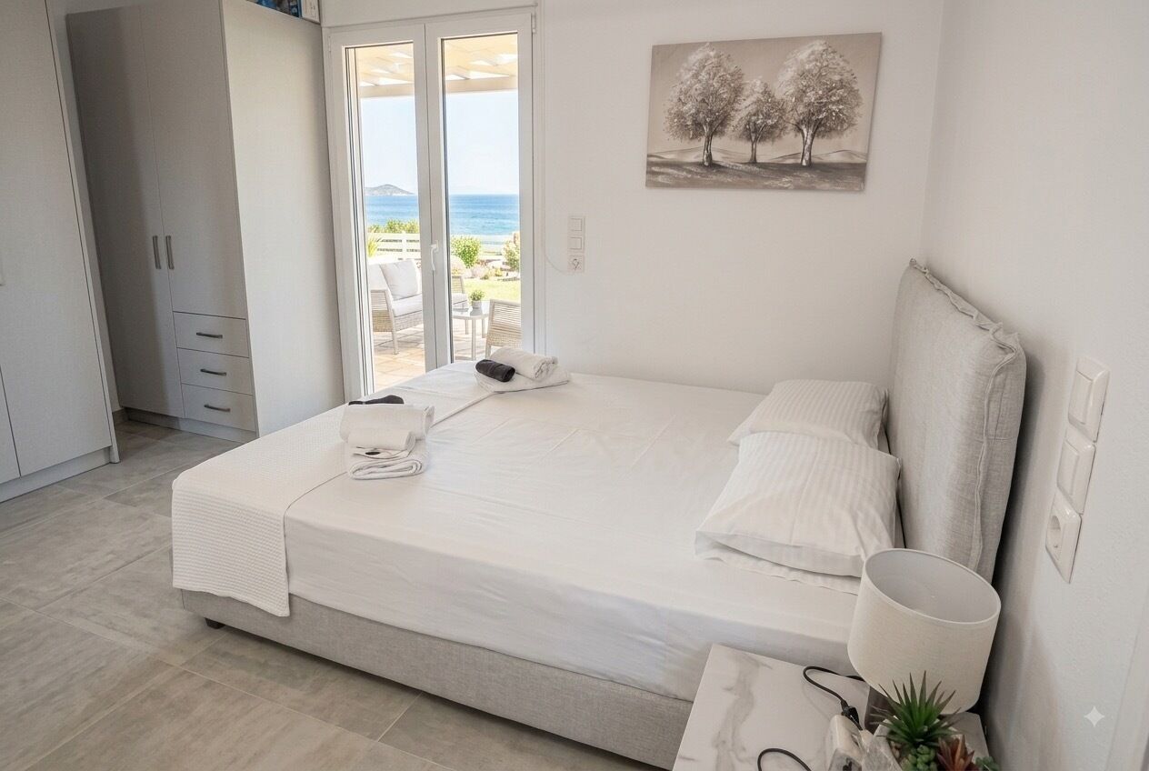 A bedroom with a bed, a bedside table with a lamp, a painting on the wall, and a view of the outdoors through a sliding door.