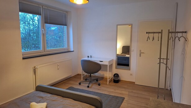 A bedroom with a bed, a desk, a mirror, a radiator, and a window. - Room "grey" in shared flat - central and quiet - VW, Autostadt, VfL parking lot and WLAN (Wolfsburg)