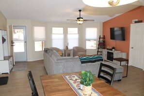 A living room with a sofa, a dining table with chairs, a ceiling fan, a TV mounted on the wall, and a kitchen area with cabinets and a microwave. - SUNDIAL RETREAT 3BR 2B House with EV Charging, Hot tub, Large Deck, and Firepit (Sedona)