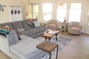 Ein Wohnzimmer mit grauem Sofa, zwei Sesseln, einem Couchtisch und einem Teppich.