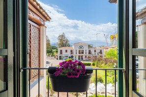 A balcony with a black planter containing purple flowers, a view of a building with a tiled roof, and a clear sky. - House in Arbatax with parking near the sea (Arbatax)