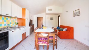 Una cucina moderna con mobili bianchi, uno schienale piastrellato e un'area pranzo con un tavolo e sedie in legno.