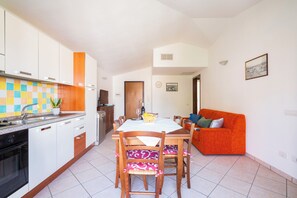 A modern kitchen with white cabinets, a tiled backsplash, and a dining area with a wooden table and chairs. - House in Arbatax with parking near the sea (Arbatax)