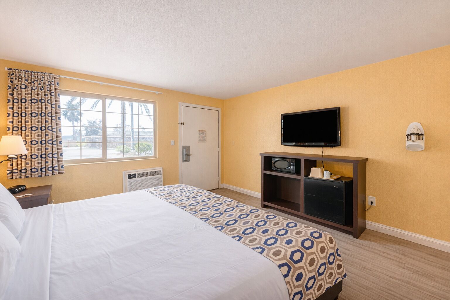 Een hotelkamer met een bed, een televisie, een magnetron en een deur.