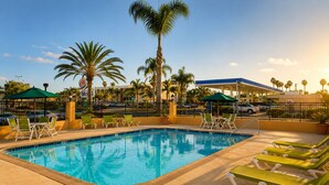 A swimming pool with lounge chairs, palm trees, and a gas station in the background. - Aurelia Oceanside (Oceanside)