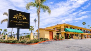 A hotel with a prominent sign, a yellow building, and palm trees. - Aurelia Oceanside (Oceanside)
