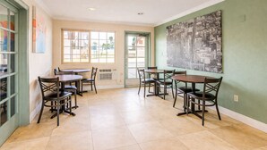A dining area with tables and chairs, a large window, and a cityscape mural on the wall. - Aurelia Oceanside (Oceanside)
