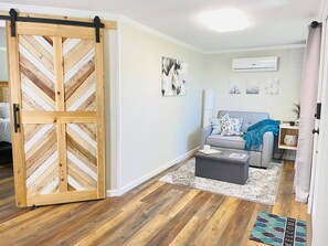 A room with a sliding wooden door, a grey sofa, a coffee table, and a rug.