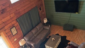 A log cabin interior with a large sofa, two armchairs, a TV mounted on a green wall, and a wooden ceiling. - The Green Bear Cabin (Unit A) Near Jellystone/Three Bears Resort in Warrens, WI (Warrens)