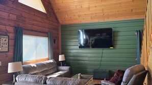 A cozy cabin interior with a wooden ceiling, a television mounted on a green wall, and a sofa set. - The Green Bear Cabin (Unit A) Near Jellystone/Three Bears Resort in Warrens, WI (Warrens)