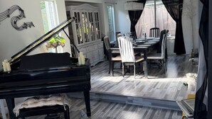 Ein Zimmer mit Klavier, Esstisch, Stühlen und einem Fenster.