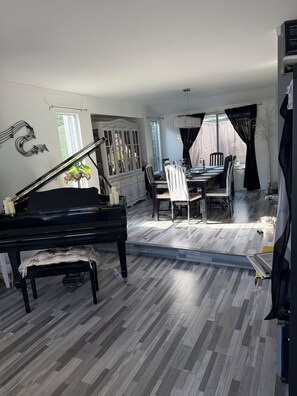 Ein Zimmer mit Klavier, Esstisch, Stühlen und einem Fenster.