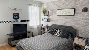 Ein Schlafzimmer mit einem Bett, einem Fernseher, einer Ablage mit Dekoration, einer Uhr und einem Schild an der Wand.