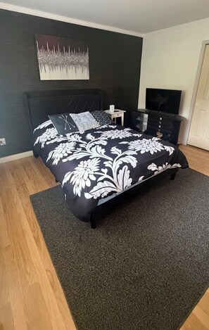 Une chambre moderne avec une couvre-lit à motifs floraux noir et blanc, un téléviseur à écran plat et un mur foncé orné d’un tableau.