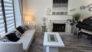 Ein Wohnzimmer mit einer Couch, einem Couchtisch, einem Kamin, einem Klavier und einem großen Fenster mit Jalousien.