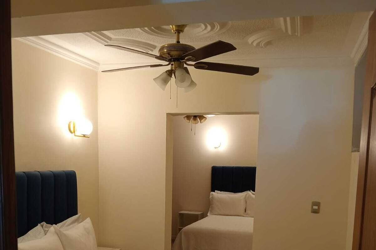 Una habitación de hotel con una cama, un ventilador de techo y una mesita de noche.